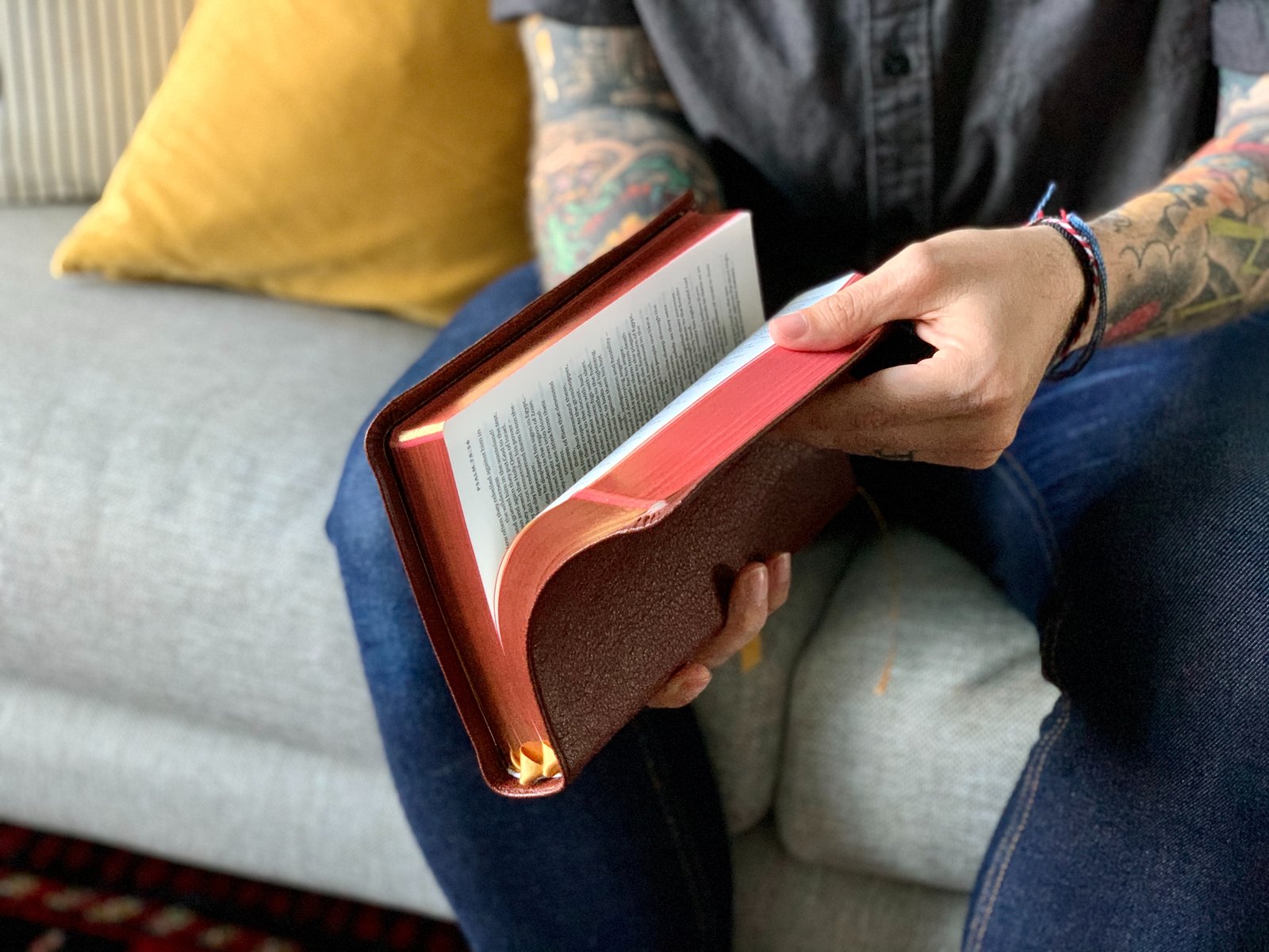 person in blue denim jeans holding red and white book